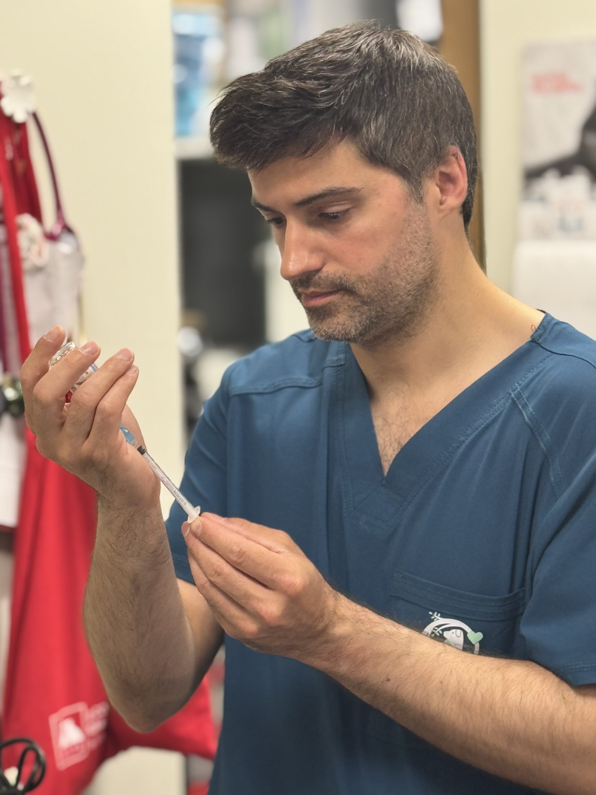 Veterinario con scrubs azules preparando una jeringa en clínica veterinaria