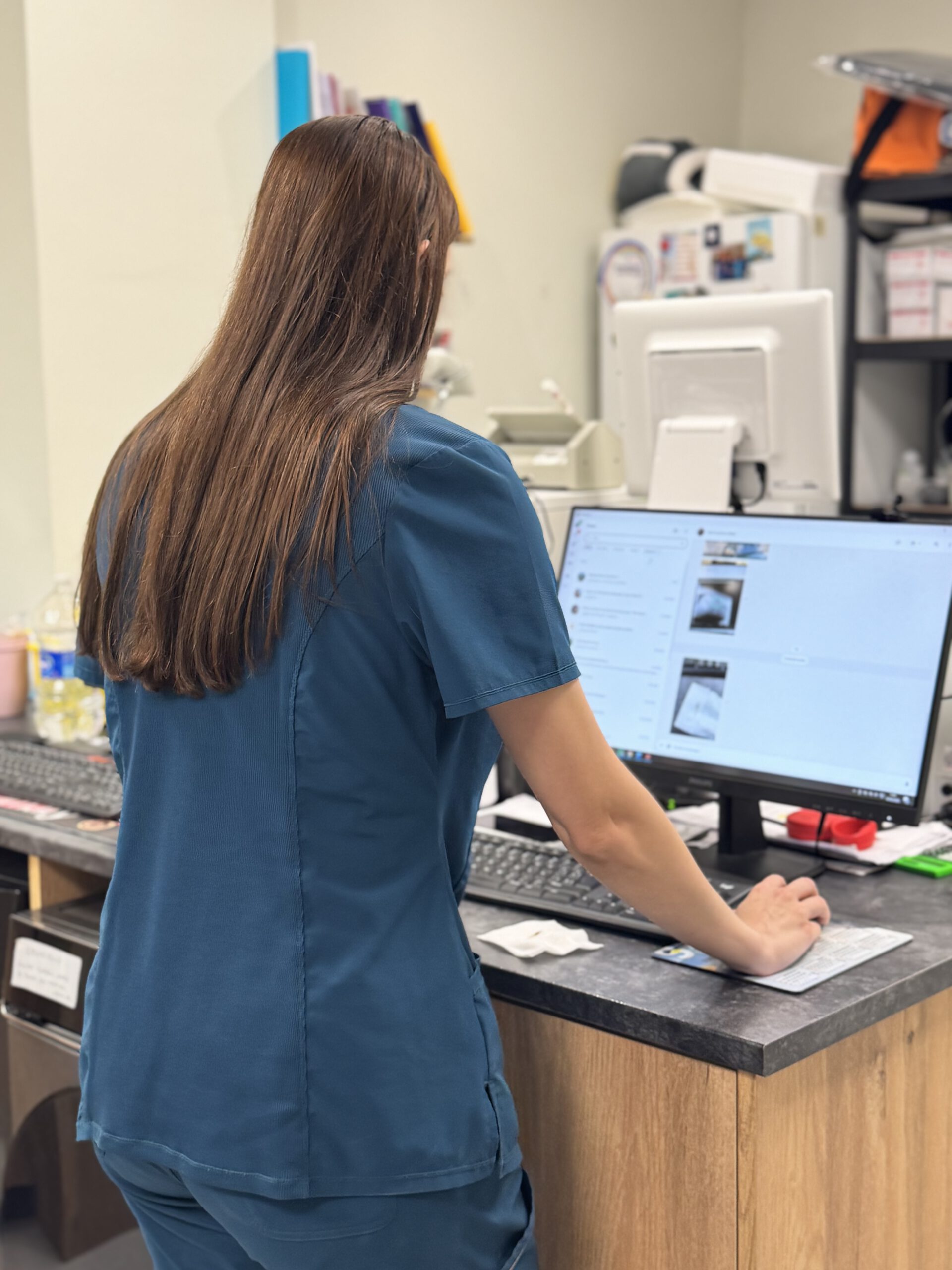 Enfermera con uniforme azul trabajando en computadora en estación de trabajo médica